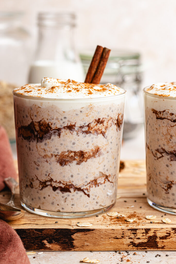 Cinnamon roll overnight oats served in a glass topped with yoghurt and a dusting of cinnamon.