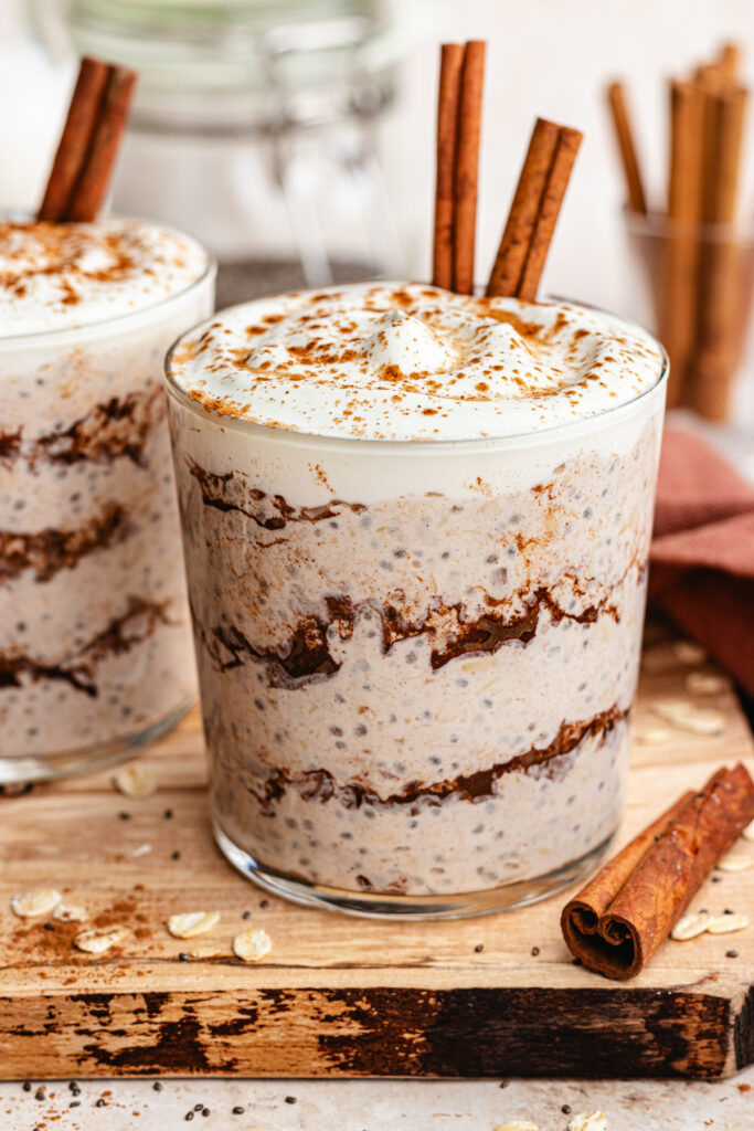 Cinnamon roll overnight oats served in a glass topped with yoghurt and a dusting of cinnamon.