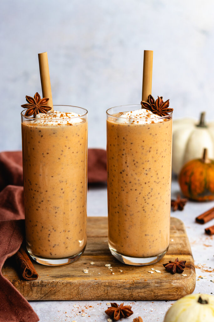 Healthy pumpkin smoothie served in two tall glasses with straws. They are topped with yoghurt and a dusting of cinnamon.