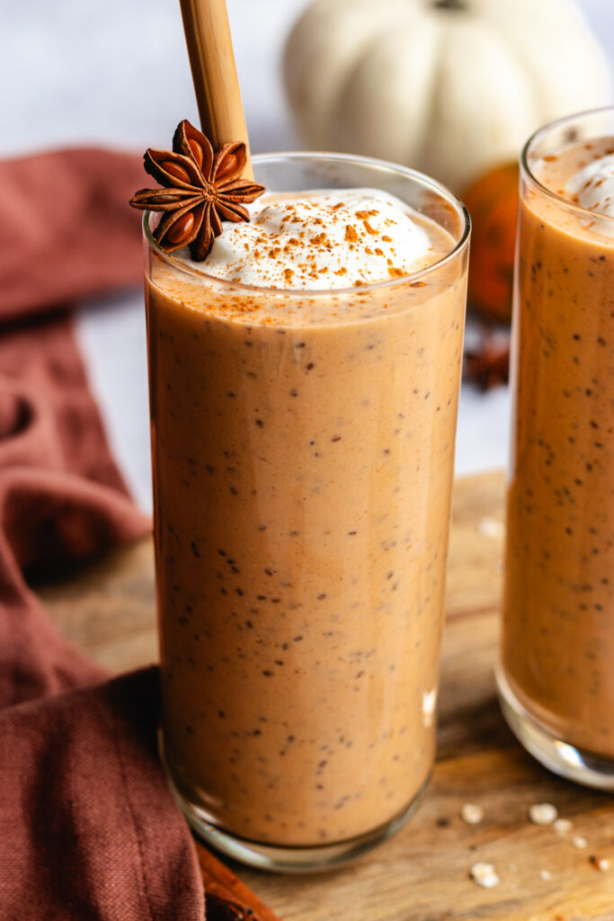 Healthy pumpkin smoothie served in a tall glass with a straw and topped with yoghurt and a dusting of cinnamon. 
