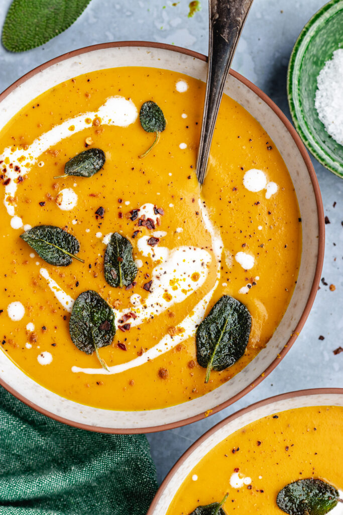 Roasted butternut squash and carrot soup served in 2 bowls. Topped with coconut milk, sage and spices.
