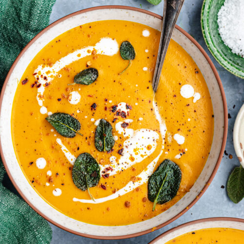 Roasted butternut squash and carrot soup served in 2 bowls. Topped with coconut milk, sage and spices.