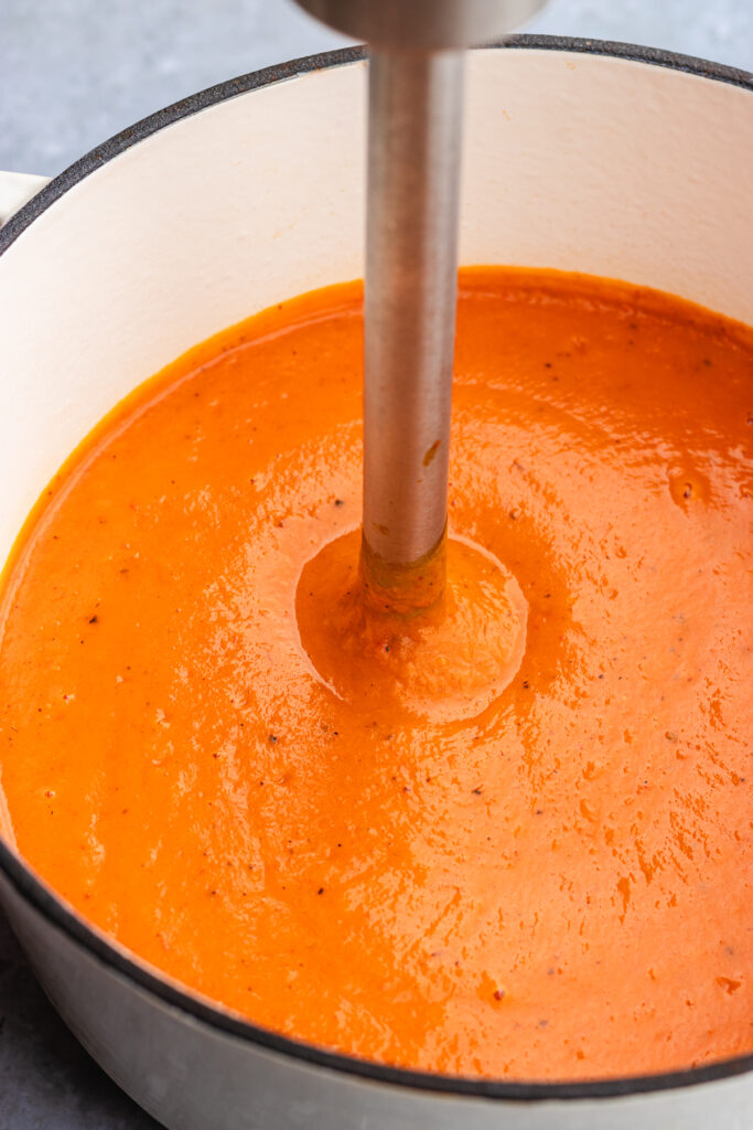 The soup being blended until smooth with a hand held blender.