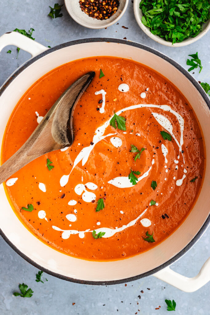 Roasted sweet potato and red pepper soup in a large pot. Topped with a drizzle of cream and some parsley and chili flakes.