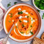 Roasted sweet potato and red pepper soup served in a bowl. topped with a drizzle of cream and some parsley and chili flakes.