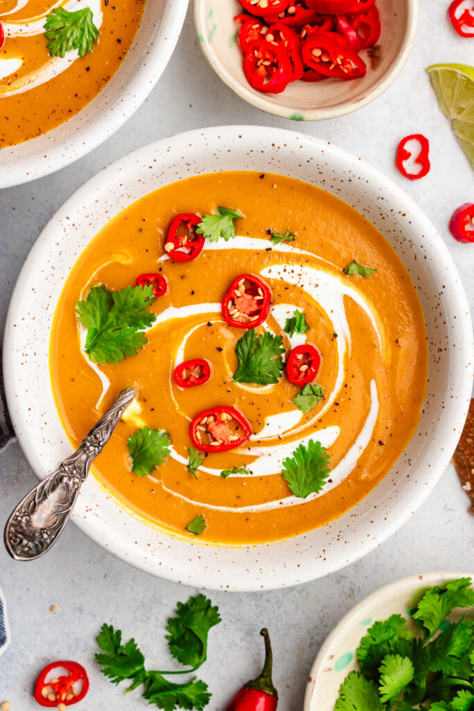 Sweet potato, coconut and chilli soup served in two bowls. Topped with cream, sliced chilli and cilantro.