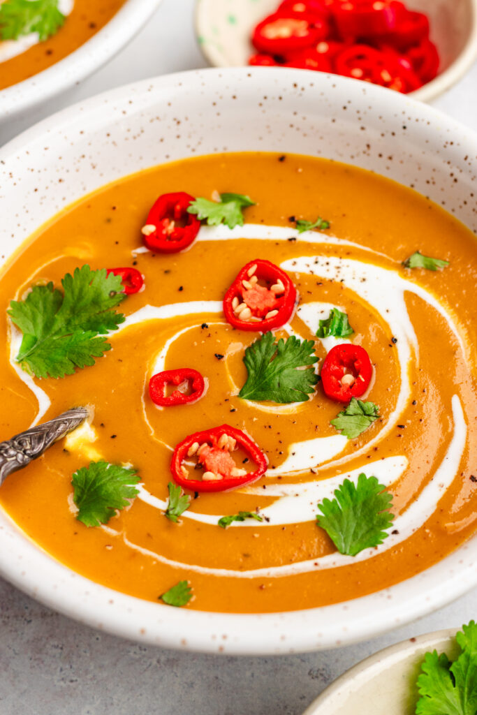 Sweet potato, coconut and chilli soup served in two bowls. Topped with cream, sliced chilli and cilantro.