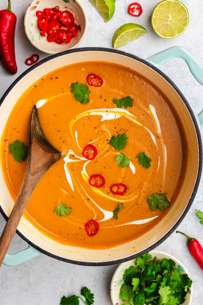 Sweet potato, coconut and chilli soup served in a large soup pot. Topped with cream, sliced chilli and cilantro.