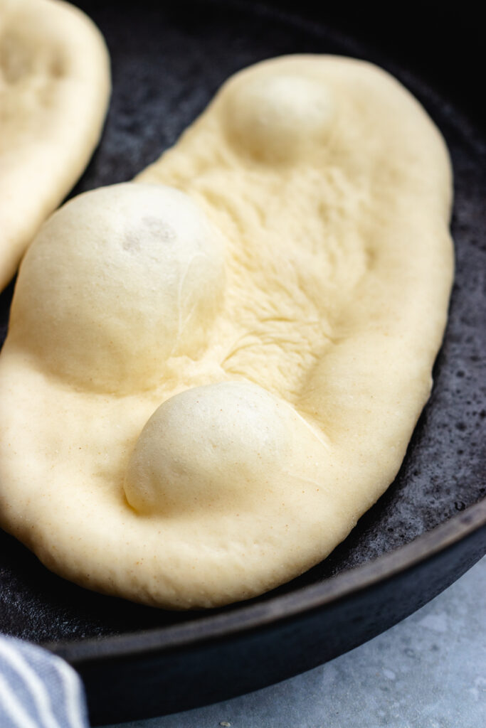 The naan bread cooking in a frying pan. 
