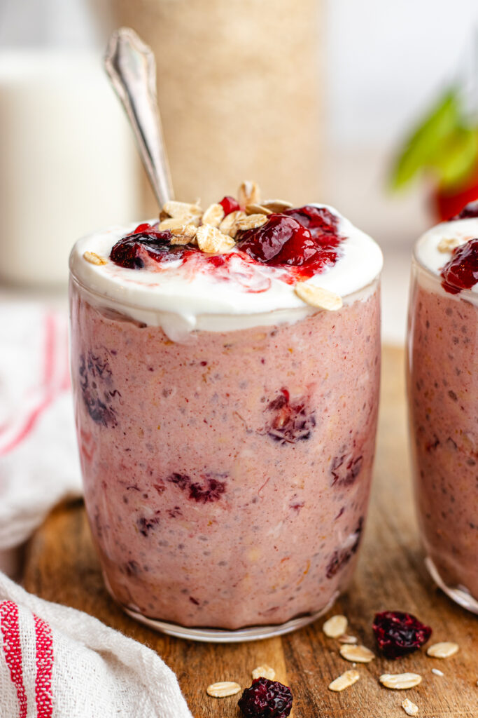 Cranberry overnight oats served in a glass topped with yoghurt and cranberry sauce.