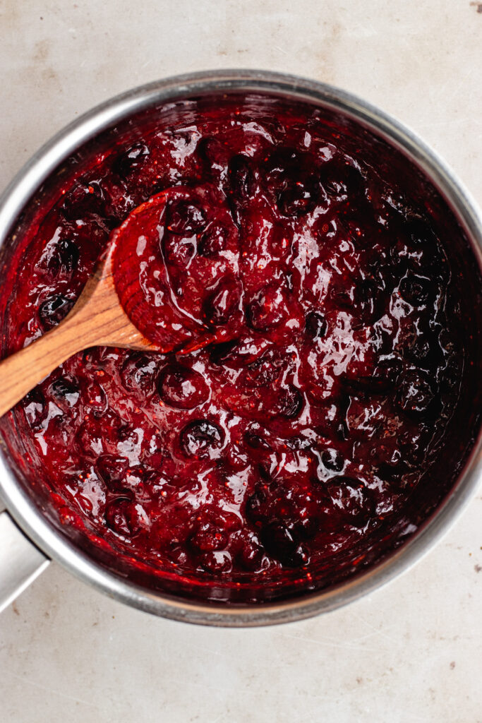 The finished cranberry sauce in the pot with a wooden spoon. 