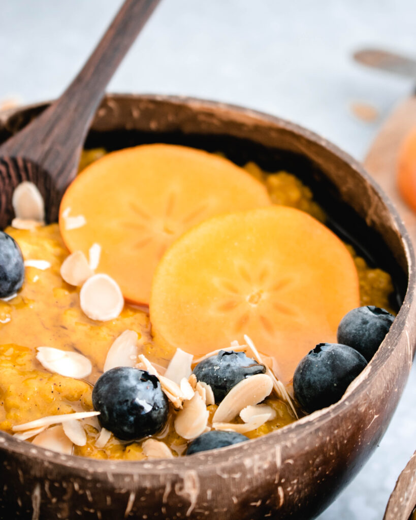Persimmon Oatmeal served in a bowl topped with slices of fresh persimmon and blueberries.
