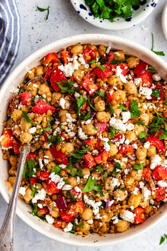 Lentil and chickpea salad served in a bowl topped with feta cheese and parsley. 