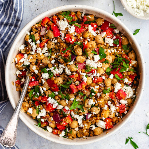 Lentil and chickpea salad served in a bowl topped with feta cheese and parsley.