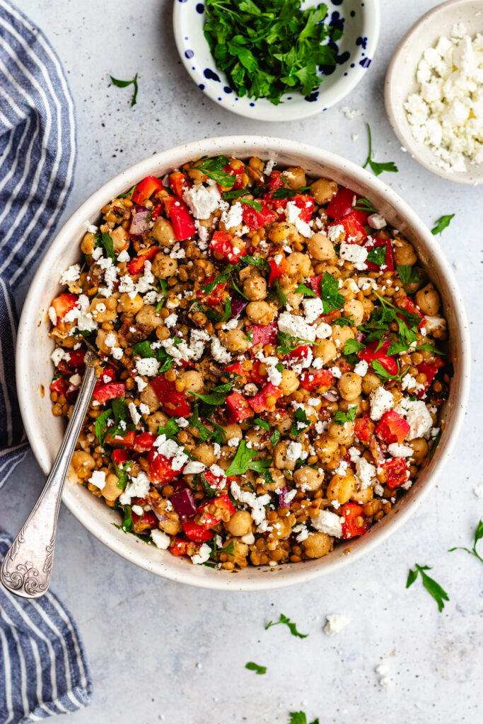 Lentil and chickpea salad served in a bowl topped with feta cheese and parsley.