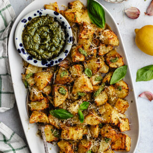 Pesto roasted potatoes on a serving platter topped with pesto and parmesan.