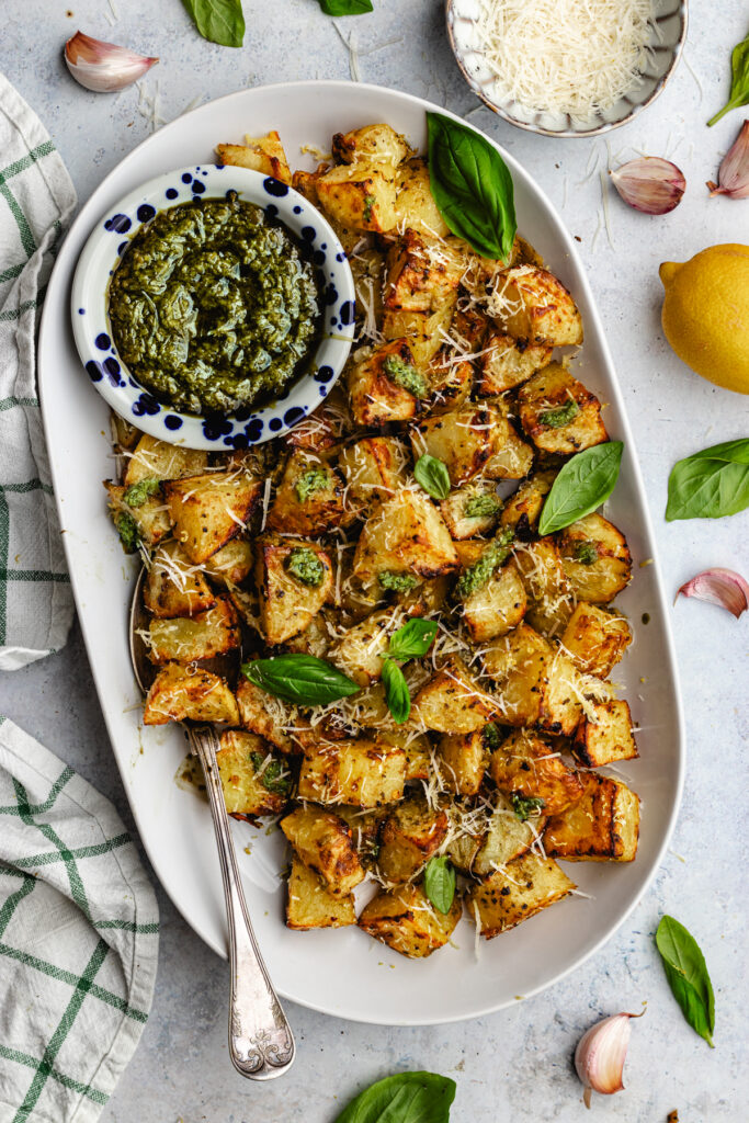 Pesto roasted potatoes on a serving platter topped with pesto and parmesan. 