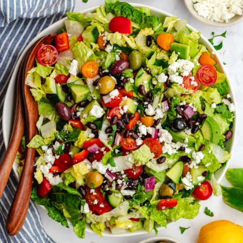 Mediterranean black bean salad served in a white bowl with a wooden salad spoon.