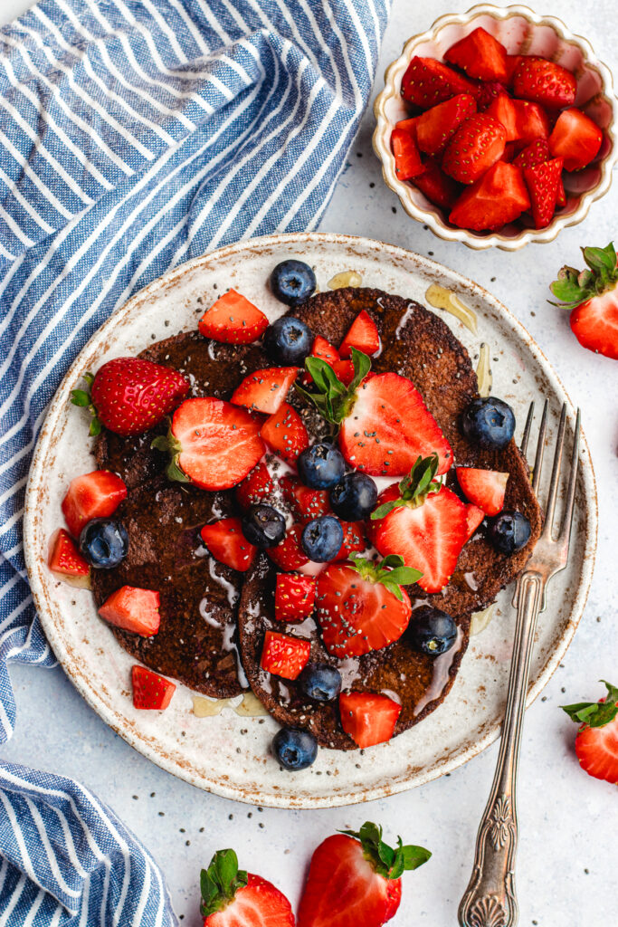 3 Ingredient Chocolate Banana Pancakes on a plate topped with berries.