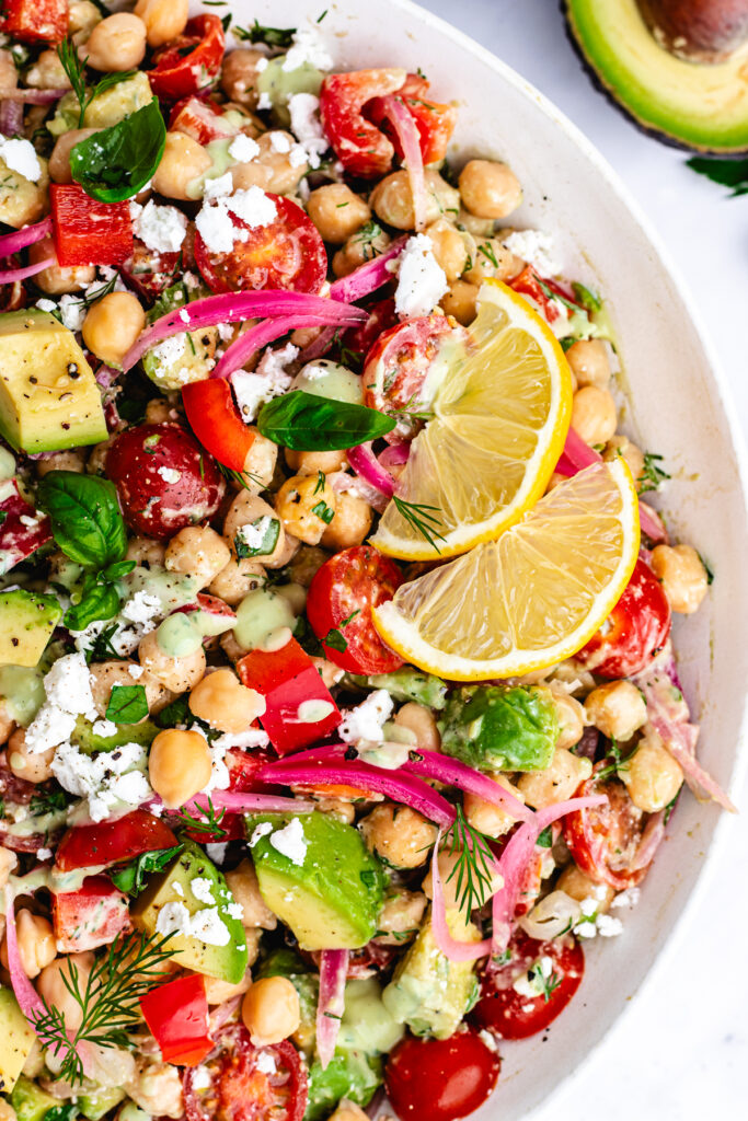 The salad in a big salad bowl topped with dressing and lemon slices.