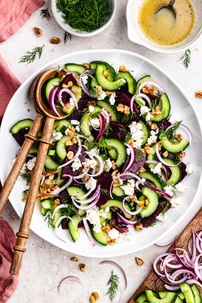 The salad in a large salad bowl topped with goats cheese, nuts and herbs.