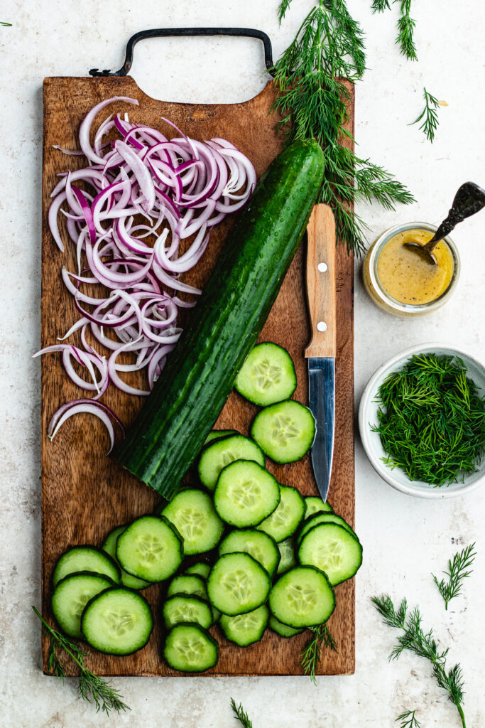 The sliced cucumbers and red onion on a cutting board.