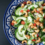 The Cucumber Salad in a salad bowl topped with cashews and fresh herbs.