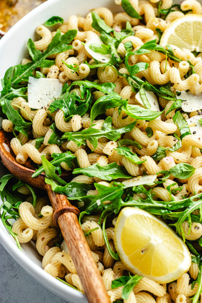 The pasta salad in the salad bowl topped with lemon slices.
