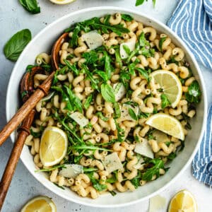 The pasta salad in the salad bowl topped with fresh basil and lemon slices.