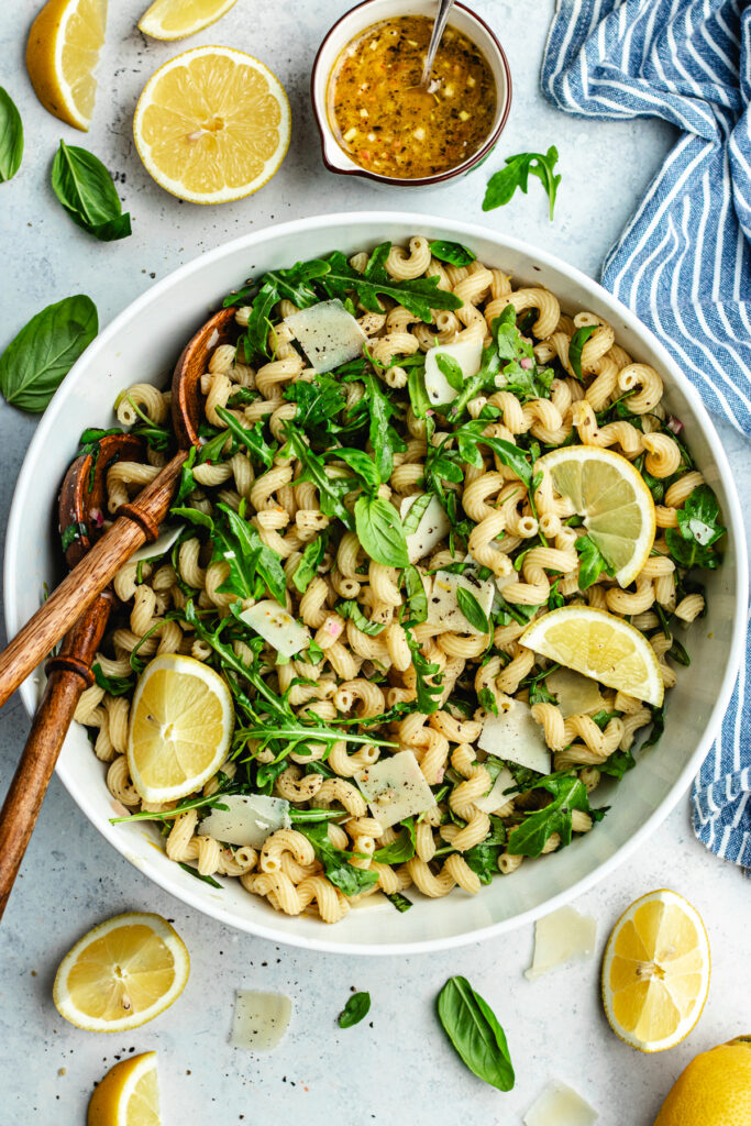 The pasta salad in the salad bowl topped with fresh basil and lemon slices.