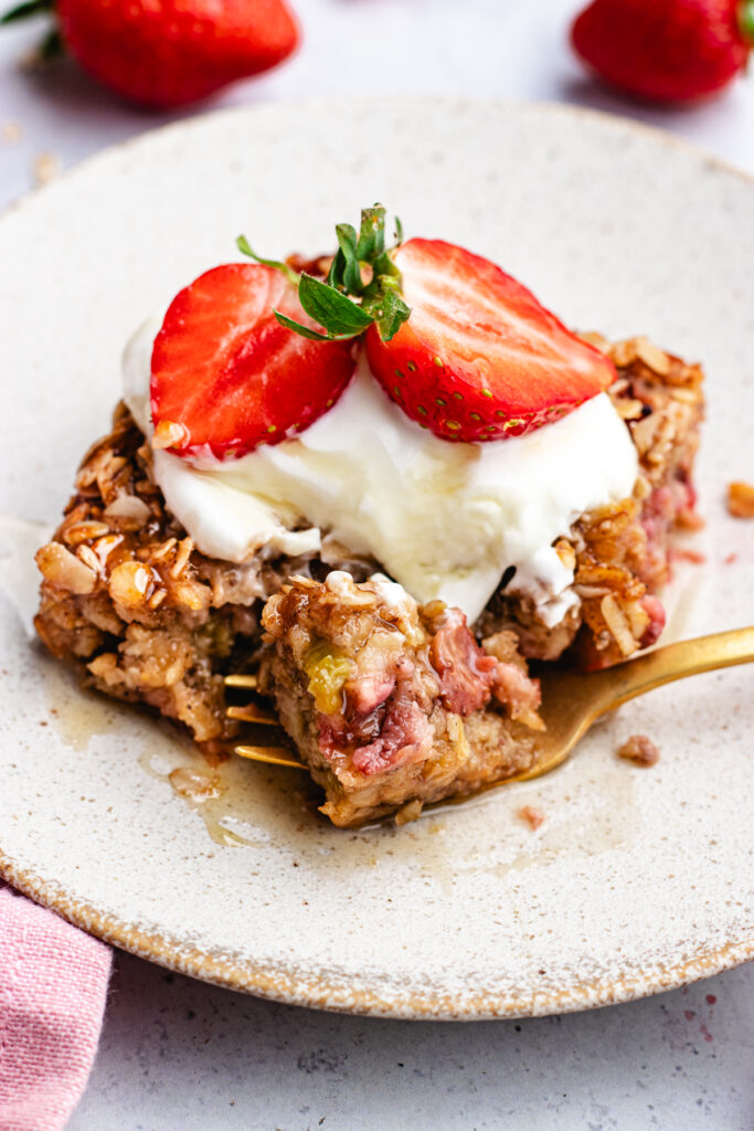 A slice of the baked oats on a small plate topped with yoghurt, strawberries and maple syrup.