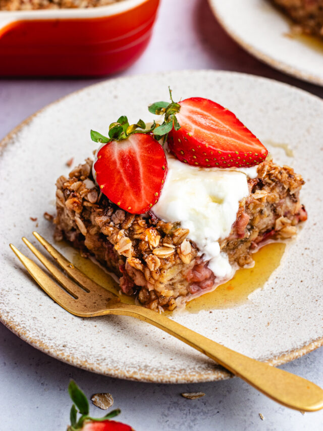 A slice of the baked oats on a small plate topped with yoghurt, strawberries and maple syrup.