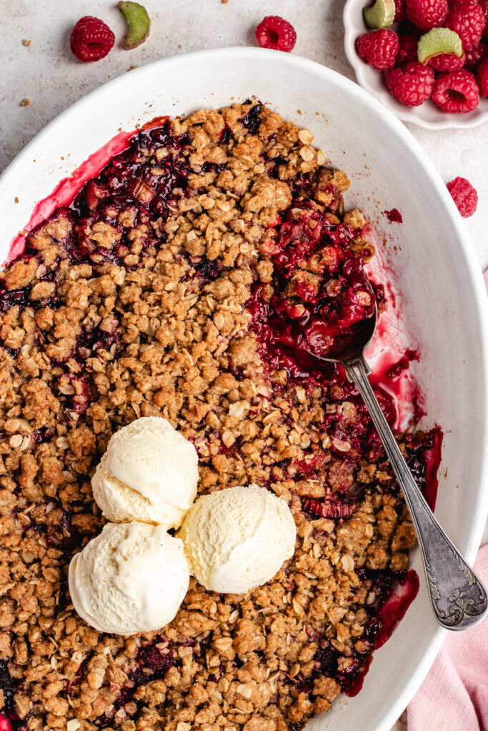 The baked crumble topped with ice cream in the baking dish with a serving spoon.