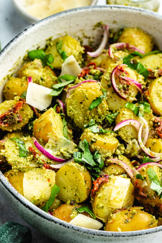 The potato salad in a bowl topped with fresh basil and parmesan cheese.