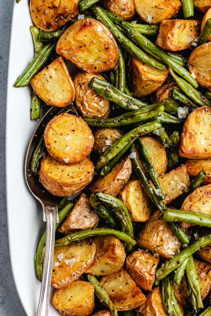 The roasted potatoes and green beans on a serving platter with a spoon.