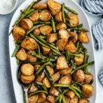 The roasted potatoes and green beans on a serving platter with a spoon.