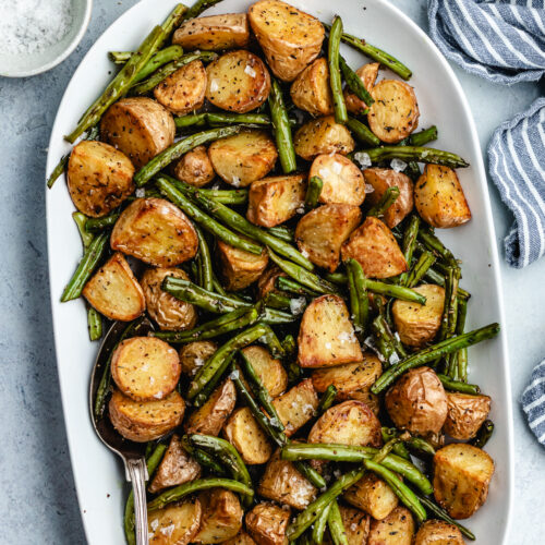 The roasted potatoes and green beans on a serving platter with a spoon.