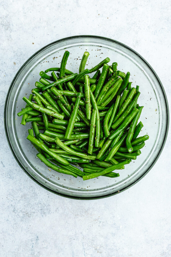 The green beans in a bowl with the oil and spices.