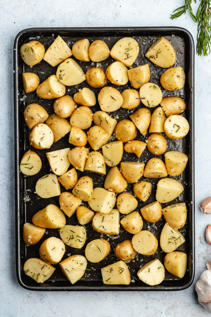 The potatoes tossed with the oil, garlic and spices on the baking sheet.