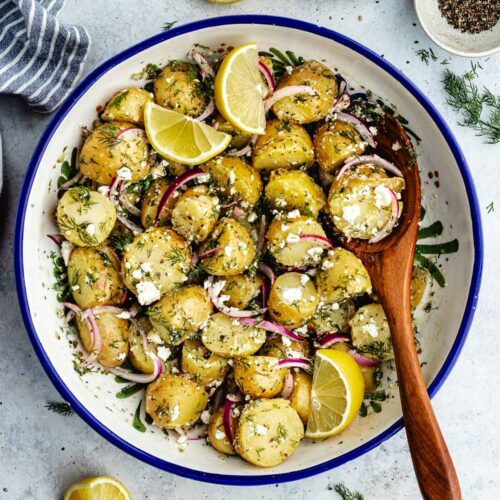 The potato salad in a bowl with a wooden spoon.