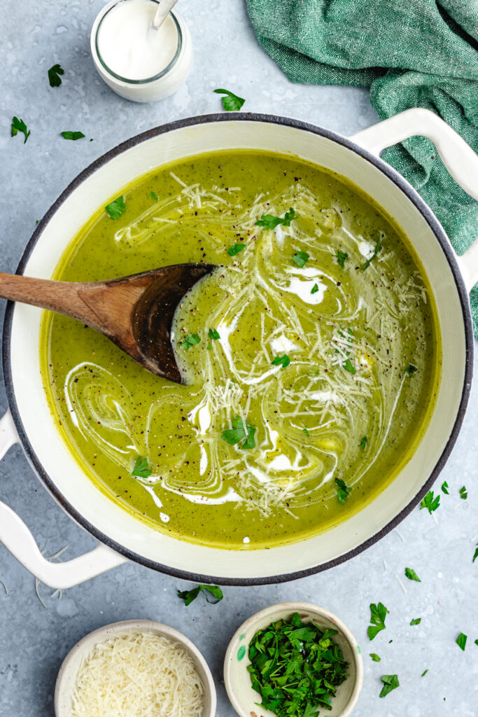 The finished soup in a pot drizzled with cream and topped with parsley and parmesan cheese.