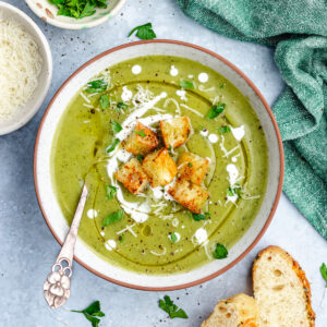The soup in a bowl topped with croutons, cream and parmesan cheese.