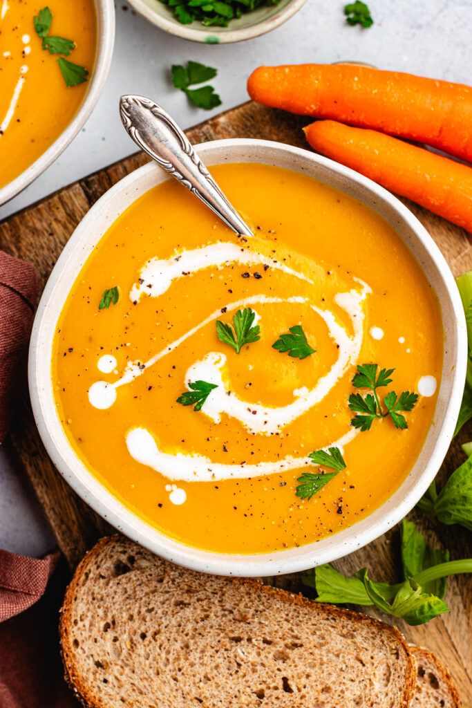 The soup in a bowl topped with some coconut milk and parsley. Served with a side of bread.