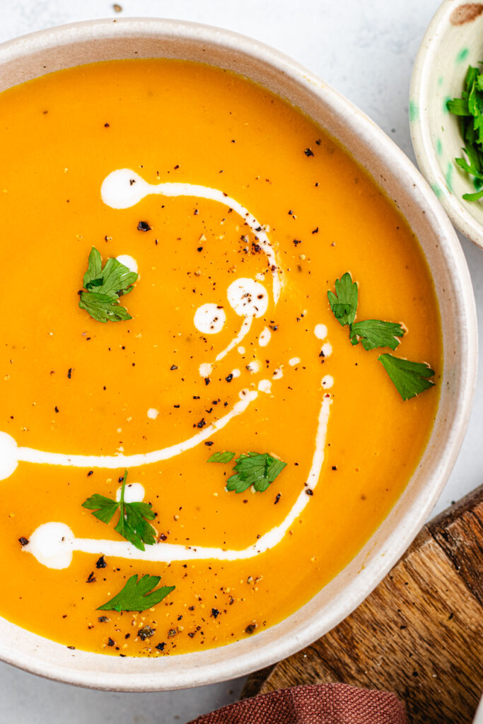 The soup in a bowl topped with some coconut milk and parsley.