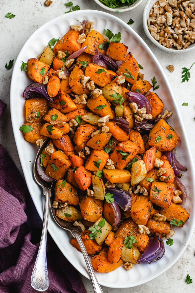 The roasted vegetables on a large serving platter topped with chopped parsley and walnuts.