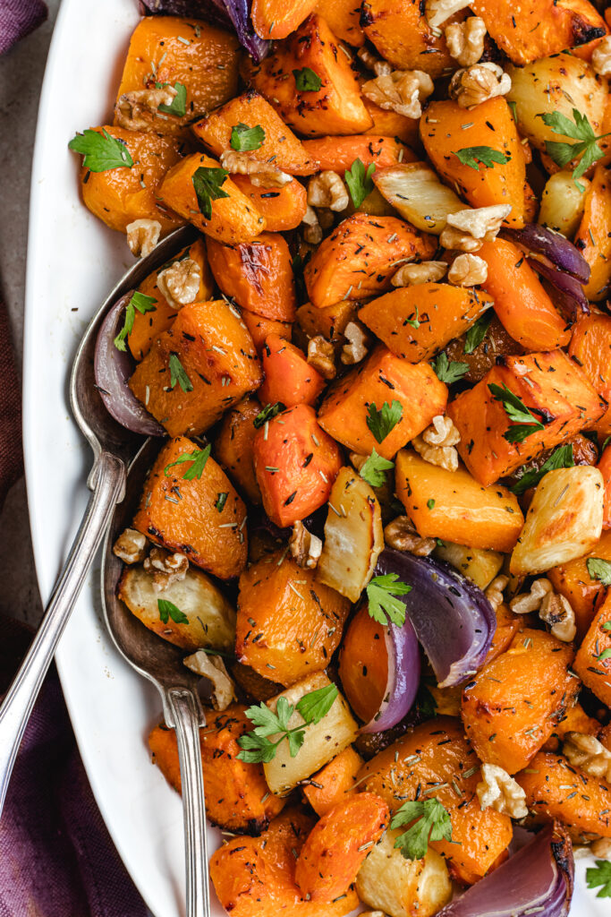 The roasted vegetables on a white serving platter topped with chopped parsley and walnuts.
