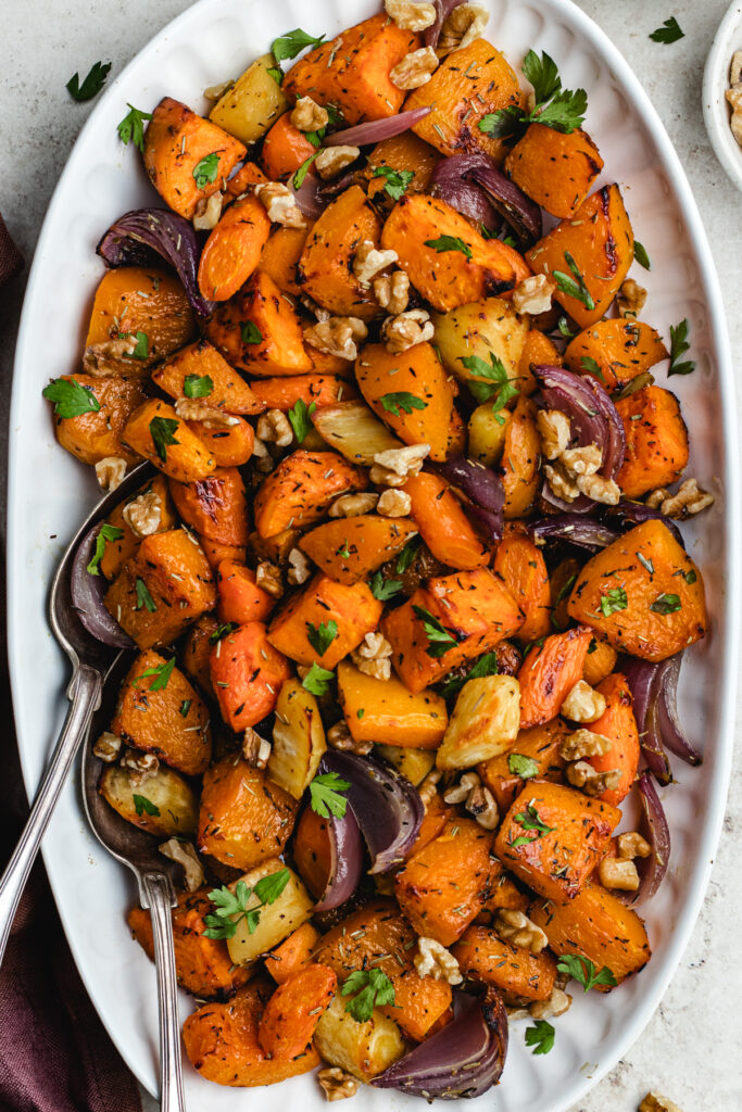 The roasted vegetables on o serving platter topped with chopped parsley and walnuts. 