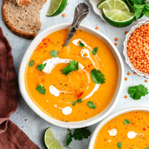 The soup in two bowls topped with a drizzle of coconut milk and chopped herbs.