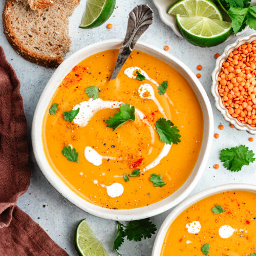 The soup in two bowls topped with a drizzle of coconut milk and chopped herbs.