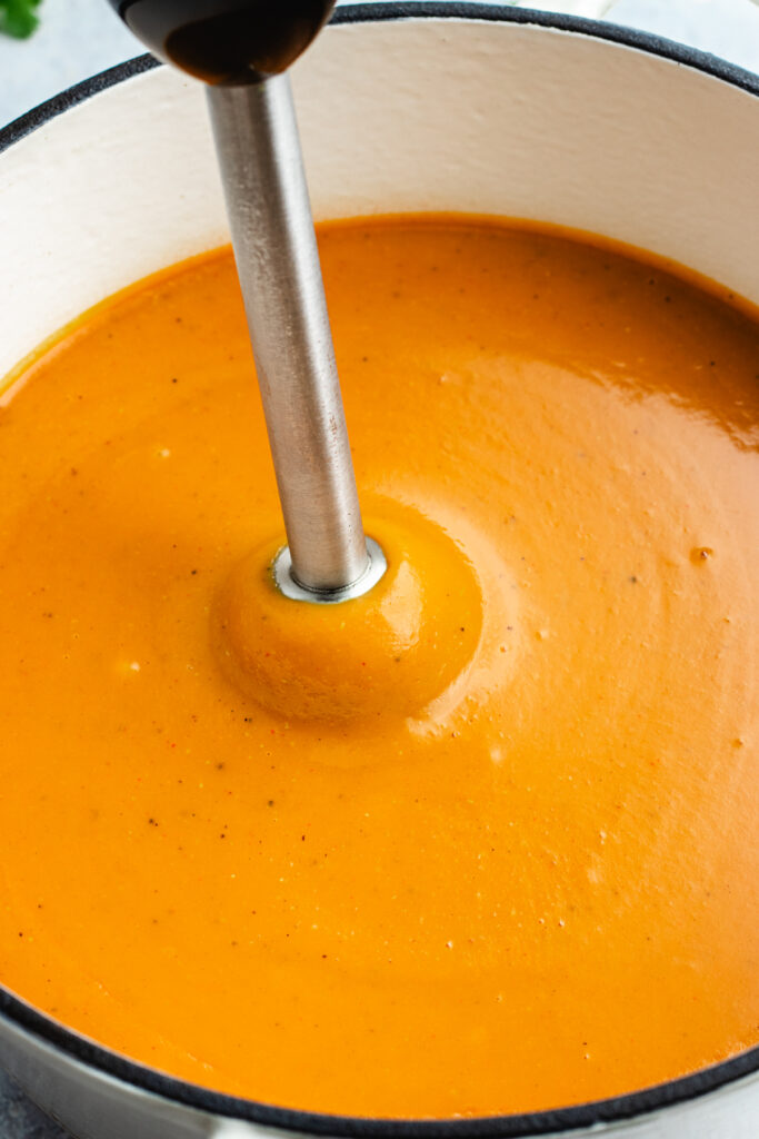 Blending the soup with an immersion blender.